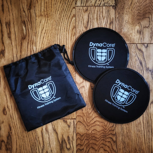 Two black floor slider discs with the DynaCore® logo on a wooden surface